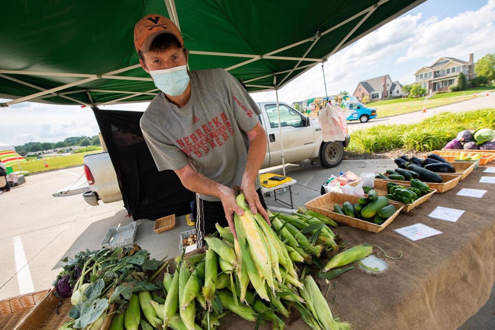 Man selling sweet corn at a Farmer's Market booth.